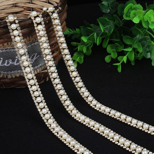 May include: Three strands of gold trim with white pearl beads and clear rhinestones.