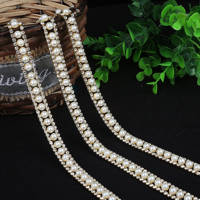 May include: Three strands of gold trim with white pearl beads and clear rhinestones.