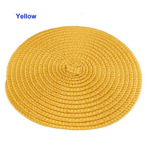 May include: A round, yellow woven placemat with a spiral design. The placemat is made of a natural material and has a textured surface. The word "Yellow" is printed in blue in the upper left corner.