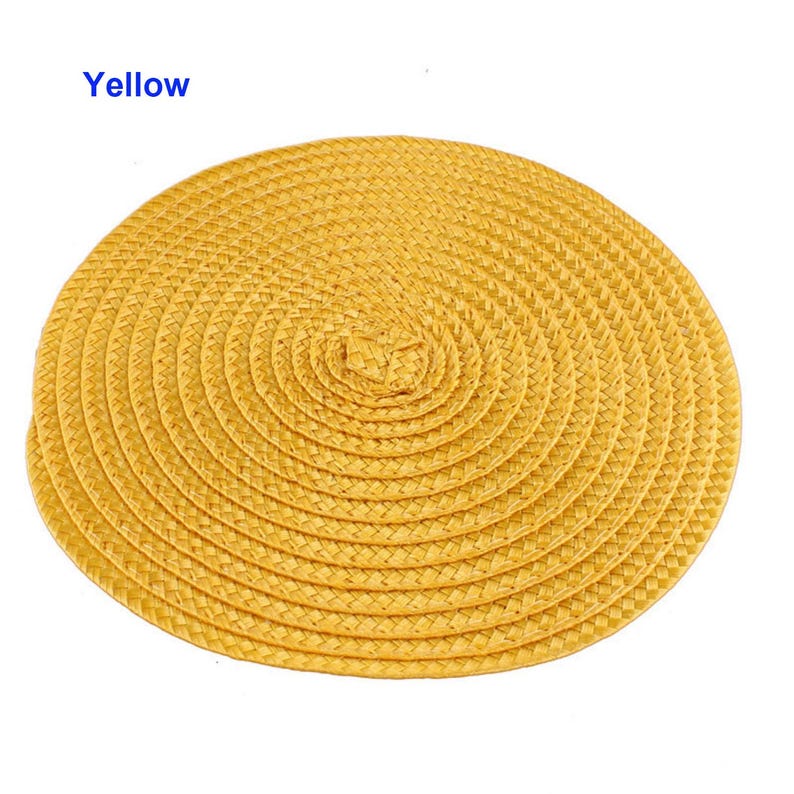 May include: A round, yellow woven placemat with a spiral design. The placemat is made of a natural material and has a textured surface. The word "Yellow" is printed in blue in the upper left corner.