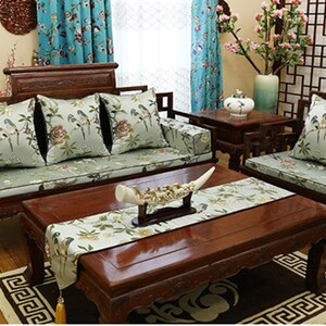 May include: A wooden sofa with green cushions and a floral pattern. The sofa is in a living room with a wooden coffee table and a wooden side table. There is a vase with flowers on the side table.