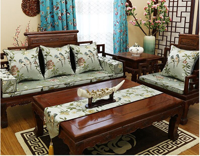 May include: A wooden sofa with green cushions and a floral pattern. The sofa is in a living room with a wooden coffee table and a wooden side table. There is a vase with flowers on the side table.
