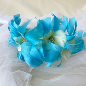 May include: A blue feather flower headband with white accents. The headband is made of feathers and is perfect for adding a touch of whimsy to any outfit.