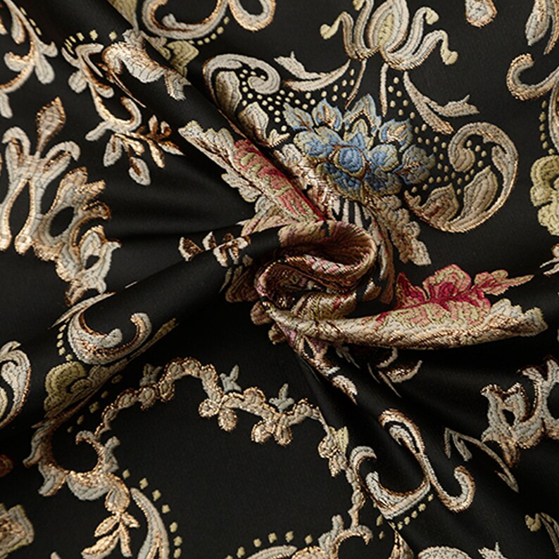May include: Black fabric with a gold and cream floral damask pattern. The fabric is woven with a raised texture.