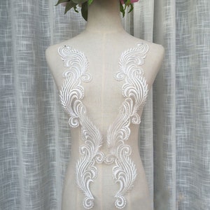 Peut inclure: Deux appliques en dentelle blanche avec un motif floral. Les appliques sont en forme de V et présentent un motif délicat et complexe.