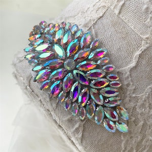 Puede incluir: Una gran decoración de cristal iridiscente con un diseño floral. Los cristales están dispuestos en un patrón radiante, con el cristal más grande en el centro. La decoración está hecha de cristales transparentes con un acabado iridiscente arcoíris.