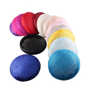 May include: A collection of colorful, round, woven hats in various shades, including purple, red, white, pink, yellow, and blue. The hats are arranged in a semi-circle, showcasing their diverse hues and textures. The hats are suitable for special occasions.