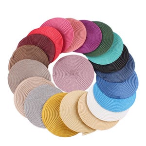 May include: A selection of circular woven placemats in a variety of colours, including pink, red, brown, purple, green, blue, and yellow. The placemats are arranged in a circular pattern, highlighting their textured surface and decorative appeal.