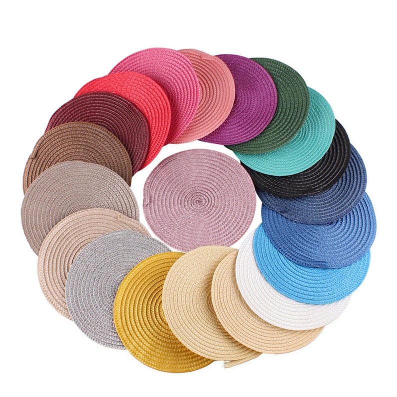 May include: A collection of colorful, round woven placemats in various shades, including pink, red, brown, purple, green, blue, and yellow. The placemats are arranged in a circular pattern, showcasing their textured surface and decorative appeal.