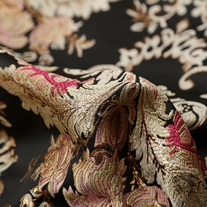 May include: Close-up of a black fabric with a gold, pink, and white floral pattern. The fabric has a textured, woven look.