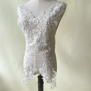 May include: White lace applique with floral and scroll designs. The applique is perfect for adding a touch of elegance to wedding dresses, bridal gowns, or other special occasion garments.