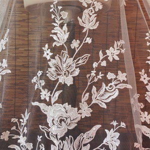 May include: White floral lace fabric with sequins. The lace features a delicate floral pattern with small sequins scattered throughout. The fabric is sheer and lightweight.