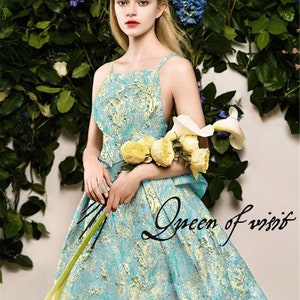 May include: A woman wearing a turquoise and gold patterned dress with spaghetti straps, holding yellow roses and white calla lilies. The text "Queen of visit" is written on the dress. The background features green foliage and blue flowers.