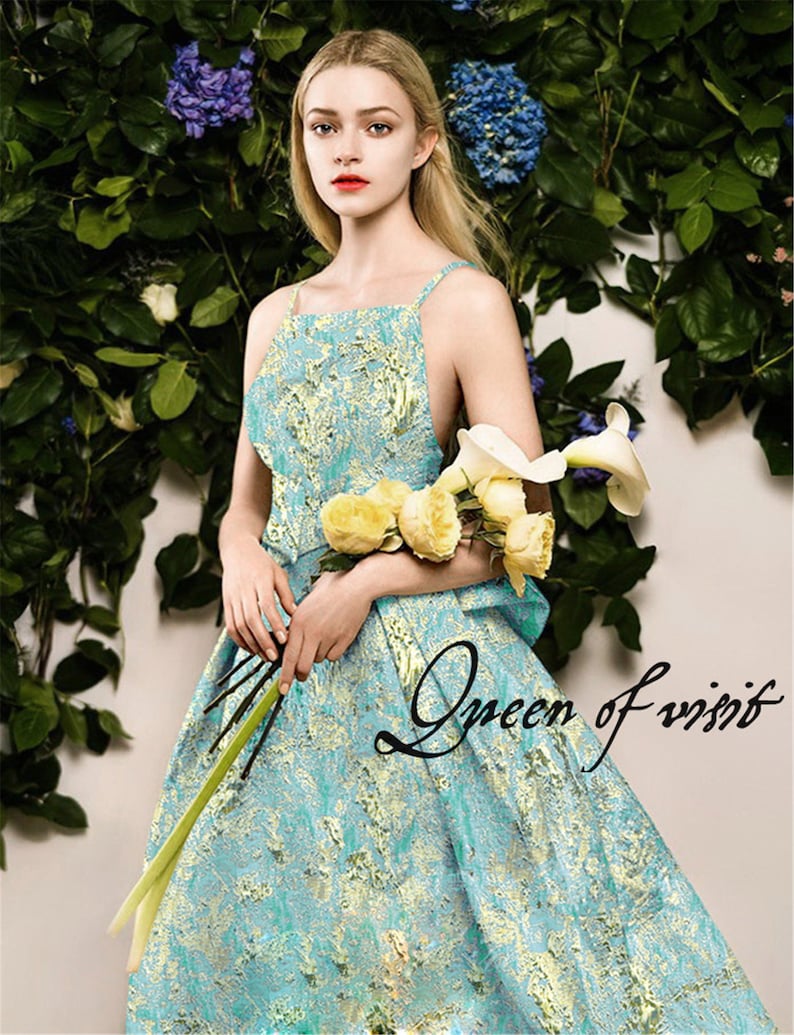 May include: A woman wearing a turquoise and gold patterned dress with spaghetti straps, holding yellow roses and white calla lilies. The text "Queen of visit" is written on the dress. The background features green foliage and blue flowers.