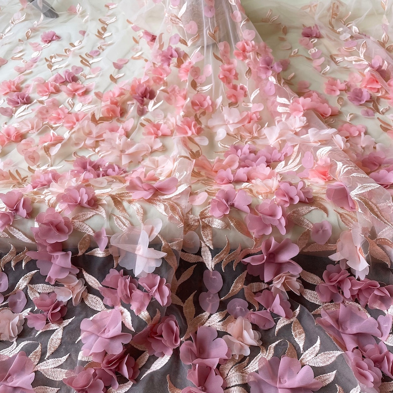 May include: Pink and gold floral lace fabric with 3D flowers. The fabric has a delicate, feminine look and would be perfect for a variety of projects, such as dresses, skirts, and tops.