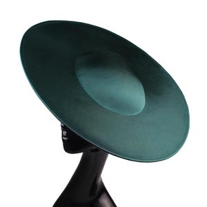 May include: A wide-brimmed hat in a deep forest green color with a smooth, satin-like finish. The hat features a rounded, shallow crown and a broad, flat brim that extends outward, displayed on a black mannequin head against a white background.