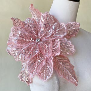 May include: Pink floral applique with sequins and beads. The applique is made of delicate fabric and has a three-dimensional design.