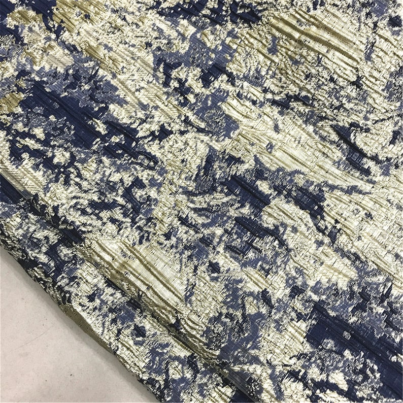 May include: Close-up of a textured fabric with a pattern of navy blue and gold. The fabric has a crinkled appearance, with diagonal lines and a mottled effect. The overall look is luxurious and elegant.