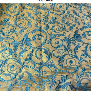 May include: A close-up of a fabric with a gold background and a blue floral pattern. The fabric has a textured, woven look.