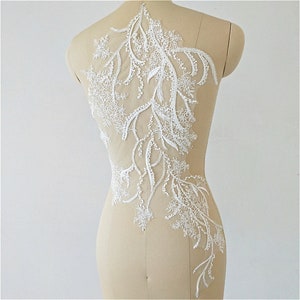 May include: White lace applique with a floral design. The lace is delicate and intricate, with a variety of small flowers and leaves. The applique is perfect for adding a touch of elegance to any garment.