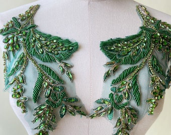May include: A pair of green beaded floral appliques with rhinestones. The appliques are on a white background and are perfect for adding a touch of elegance to any garment.