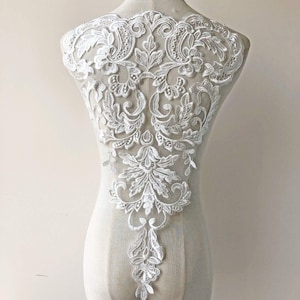 Op de afbeelding: Witte kant applique met een bloemenmotief. De kant is delicaat en ingewikkeld, met een verscheidenheid aan bloemenmotieven. De applique is perfect om een ​​toets van elegantie toe te voegen aan elk kledingstuk.