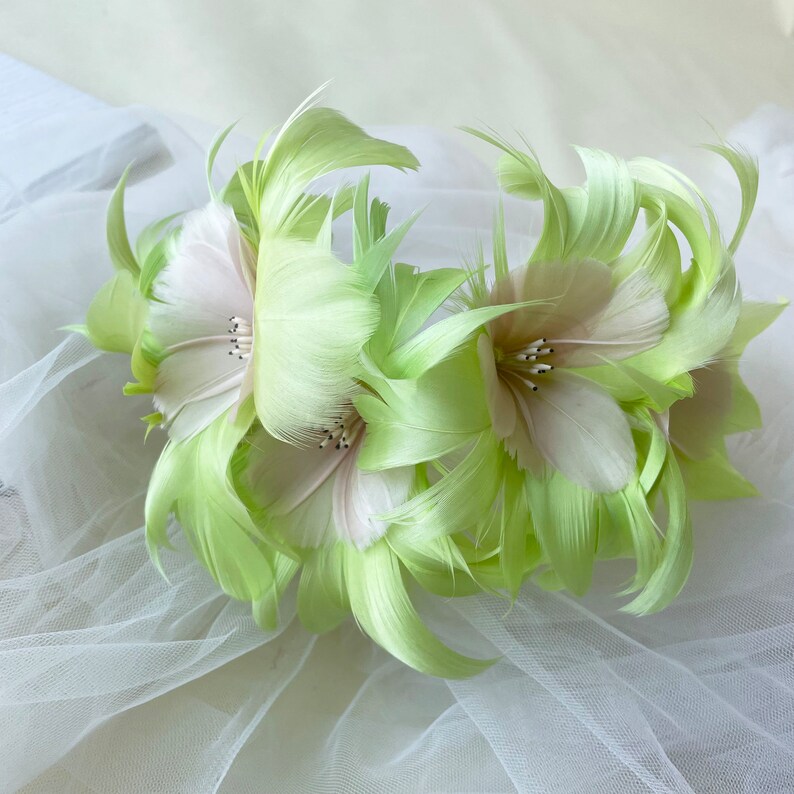 May include: A green and white feather flower crown with a delicate, layered design. The crown is made of soft, fluffy feathers and is perfect for adding a touch of whimsy to any occasion.