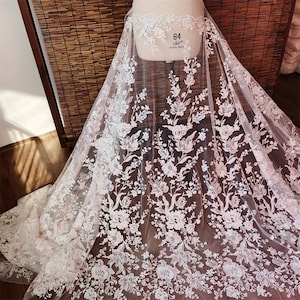 May include: White floral lace fabric with a delicate pattern. The lace is sheer and has a soft, romantic feel.