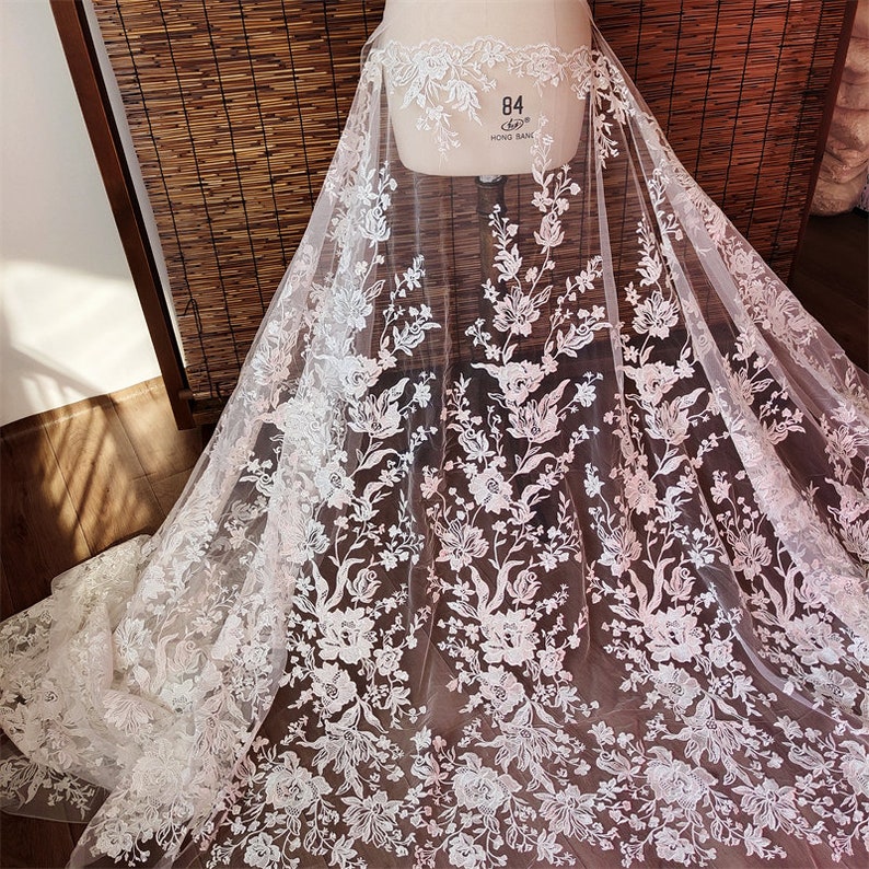 May include: White floral lace fabric with a delicate pattern. The lace is sheer and has a soft, romantic feel.