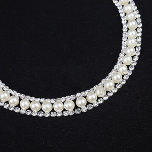 May include: A double row pearl necklace with silver rhinestone accents. The necklace is on a black fabric background.