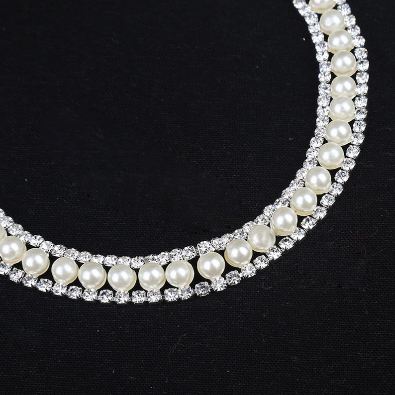 May include: A double row pearl necklace with silver rhinestone accents. The necklace is on a black fabric background.