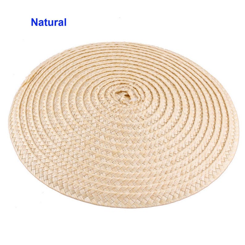 May include: A round, woven placemat in a natural beige color. The placemat is made of tightly woven straw or similar material, with a spiral pattern radiating from the center. The word "Natural" is printed in blue in the upper left corner.