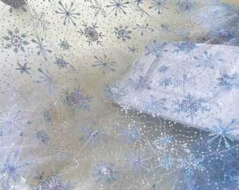 May include: White tulle fabric with a light blue snowflake pattern and iridescent sequins. The fabric is sheer and delicate.