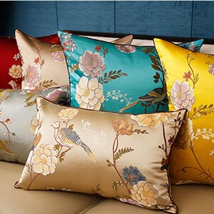 May include: A set of decorative throw pillows with floral and bird patterns. The pillows are made of satin and feature a variety of colors, including gold, teal, and cream.