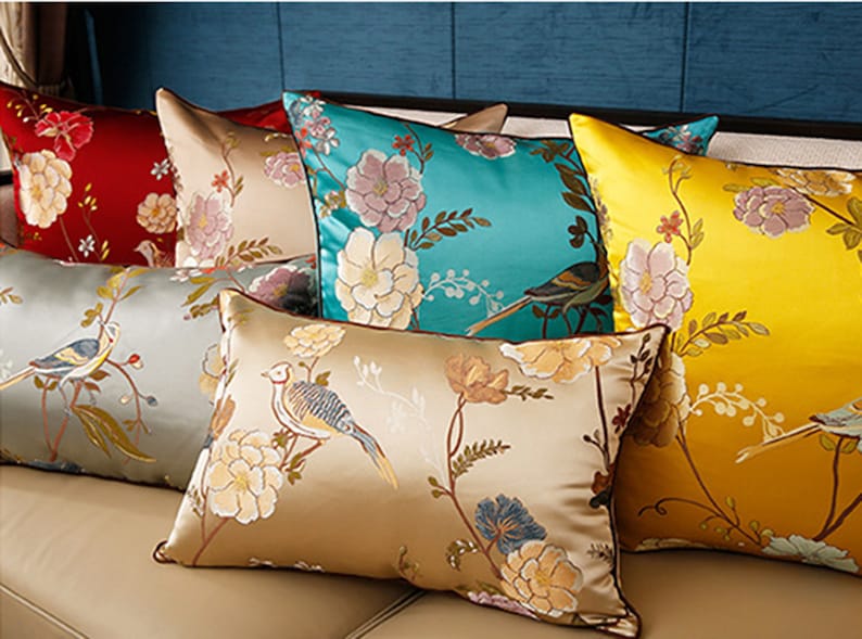May include: A set of decorative throw pillows with floral and bird patterns. The pillows are made of satin and feature a variety of colors, including gold, teal, and cream.