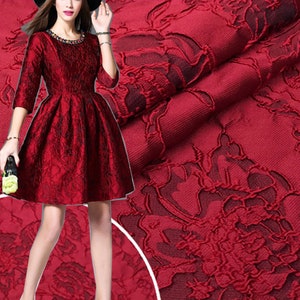 May include: Red brocade fabric with a floral pattern. The fabric has a raised texture and a soft, luxurious feel.