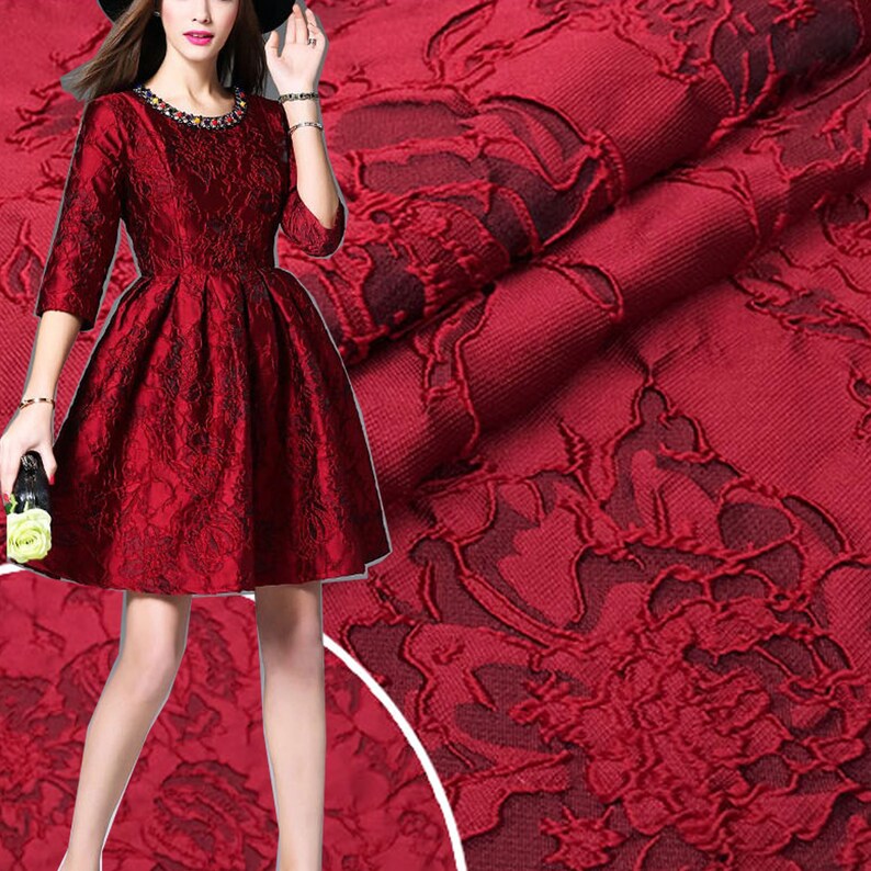 May include: Red brocade fabric with a floral pattern. The fabric has a raised texture and a soft, luxurious feel.