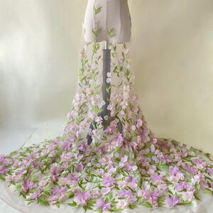 May include: A sheer white fabric with 3D pink and green floral embroidery. The fabric is draped over a dress form.