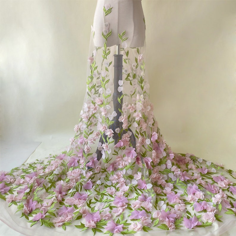 May include: A sheer white fabric with 3D pink and green floral embroidery. The fabric is draped over a dress form.
