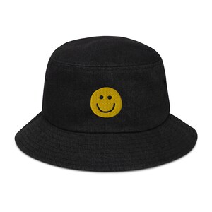 Può includere: Cappello a secchiello nero con una faccia sorridente gialla ricamata sul davanti.