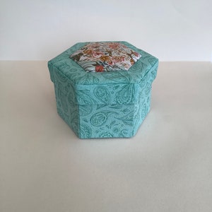 May include: A hexagonal teal box with a floral patterned lid. The box is made of fabric and has a paisley design.