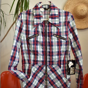 May include: A red, blue, and green plaid zip-up jacket with a large collar. The jacket has two zippered pockets on the front and a Sparz tag attached to the right sleeve.