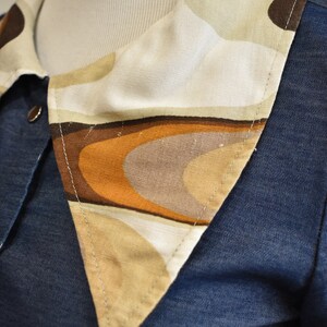May include: A blue denim shirt with a large, white, brown, and orange patterned collar. The collar is made of a soft, textured fabric and has a geometric design.