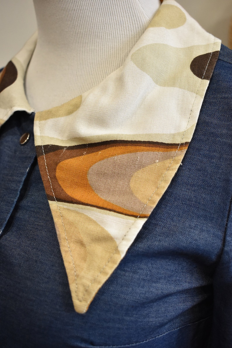 May include: A blue denim shirt with a large, white, brown, and orange patterned collar. The collar is made of a soft, textured fabric and has a geometric design.