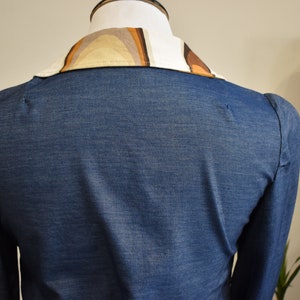 May include: A blue denim shirt with a long sleeve and a patterned collar. The collar is made of a brown and beige fabric with a geometric design.