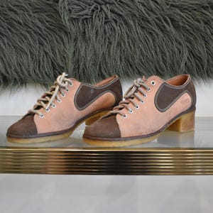 Puede incluir: Un par de zapatos de bolos de ante marrón y rosa con cordones blancos. Los zapatos tienen un tacón bajo y son de la marca "Dexter".