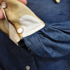 May include: Close-up of a denim shirt with a brown and white patterned cuff. The cuff has two white buttons.