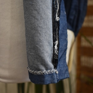 May include: Close-up of the seam of a blue denim shirt. The seam is frayed and has a white thread running through it.