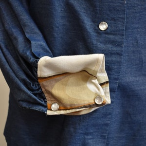 May include: A blue denim shirt with a white and brown patterned cuff. The shirt has three white buttons.