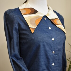 May include: A blue denim shirt with a large, white collar featuring a brown and beige geometric pattern.